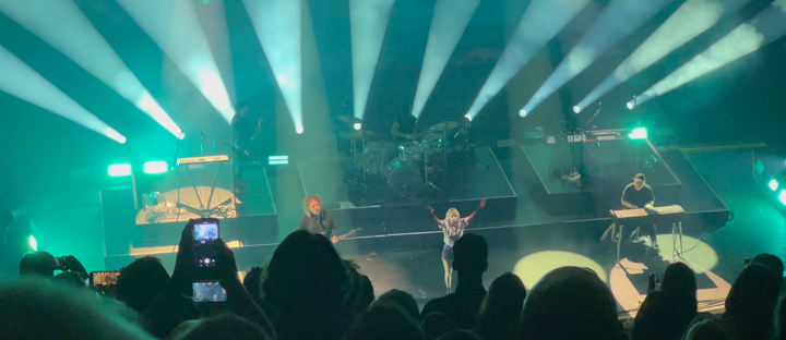 The band CHVRCHES, with frontwoman Lauren covered in fake blood, performs on a turquoise-lit stage with Robert Smith