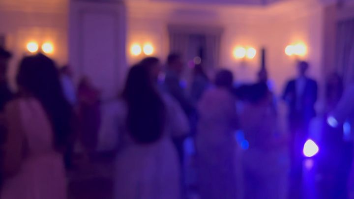 A dance floor in soft focus. People in dresses and suits are dancing.