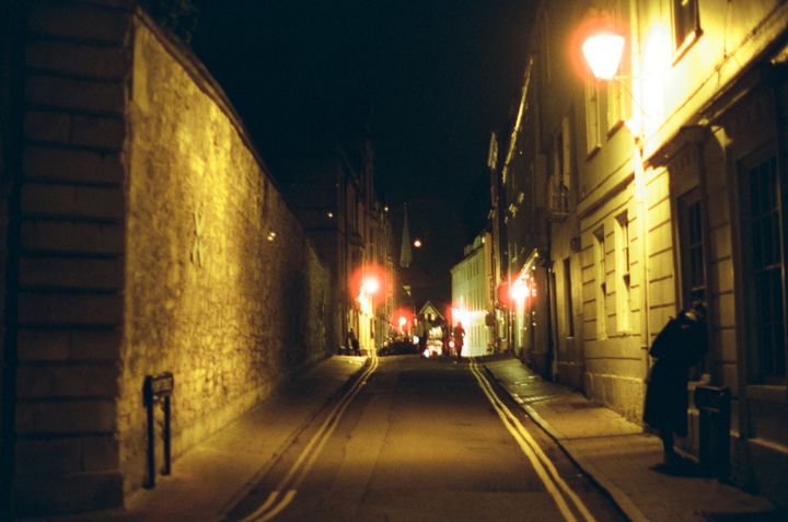 Turl Street in Oxford at night, a dark street with stone walls and old buildings, lit with street lamps.